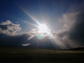Sunlight streaming on field against sky on sunny day