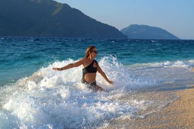 Full length of shirtless woman at beach against sky