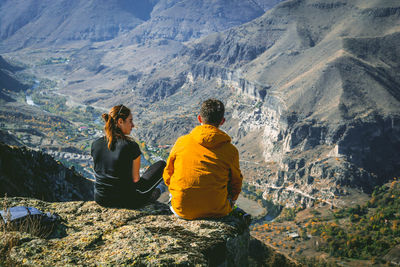 Rear view of men sitting on rock looking at mountains