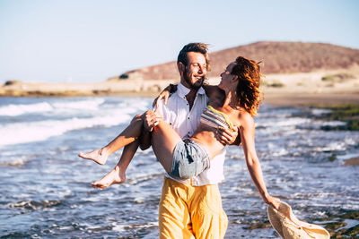 Man carrying woman while standing on beach