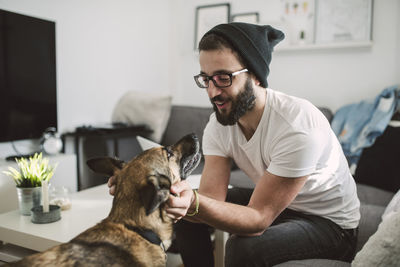 Young man at home tickling his dog