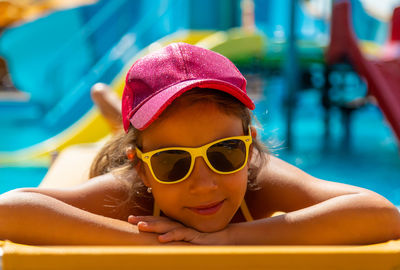 Portrait of girl wearing sunglasses lying by swimming pool