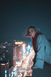 Portrait of woman standing against illuminated cityscape at night