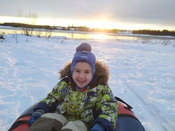 Portrait of smiling boy sitting on snow covered field