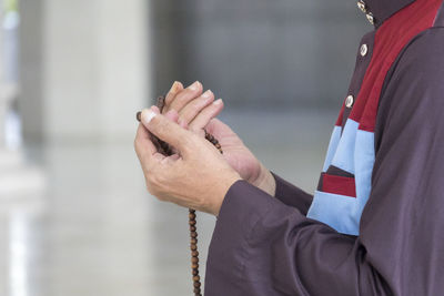 Midsection of person praying with beaded necklace