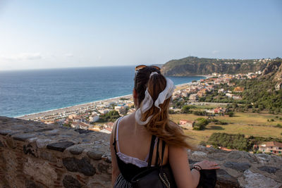 Rear view of woman looking at sea by cityscape against sky