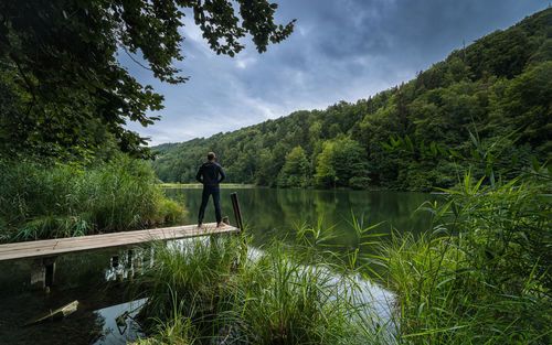 Rear view of man standing by lake against sky