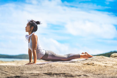 Side view of woman sitting on beach against sky