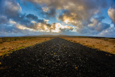 Surface level of road amidst field against sky