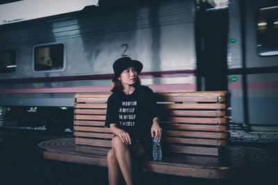 Young woman sitting on bench at railroad station platform