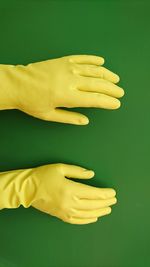 Cropped hands wearing yellow gloves over green background