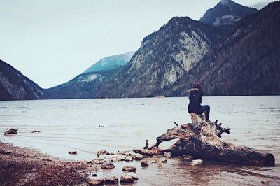 Man standing on cliff by lake against mountains