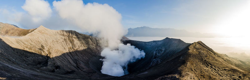 Panoramic view of smoke emitting from volcanic mountain against sky