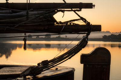 Fishing boat moored in lake against sky during sunset