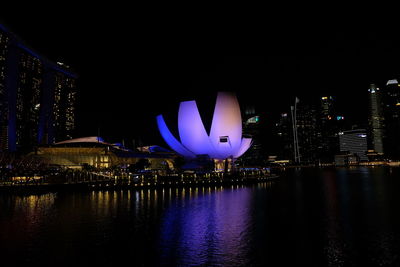 Illuminated city by river against sky at night