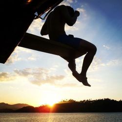 Silhouette of woman jumping in sea at sunset