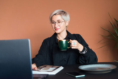 Fashion woman in black shirt working in modern work place or office with laptop and coffe cup