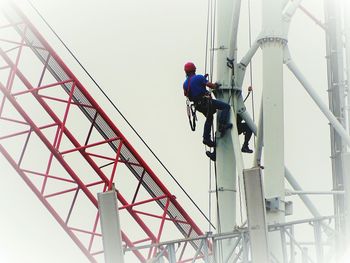 Low angle view of man working on bridge against sky