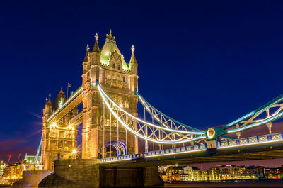 Low angle view of illuminated tower bridge against clear blue sky