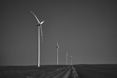 Black and white landscape with wind turbines standing on a secluded empty field with a road.