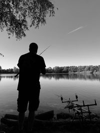 Rear view of man fishing in lake against sky