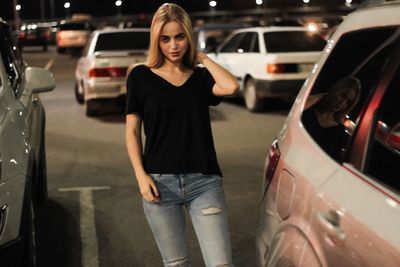 Portrait of smiling young woman standing by car at night