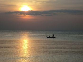 Silhouette man in sea against sky during sunset