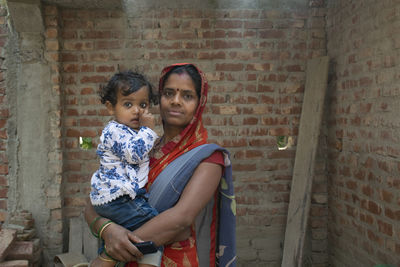 Portrait of indian mother and daughter standing against brick wall