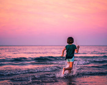 Rear view of girl on beach against sky during sunset