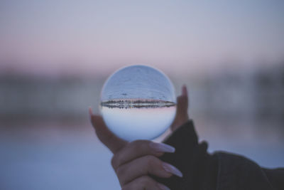 Cropped hand holding crystal ball against sky during sunset