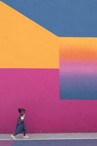 Side view of woman standing against pink wall