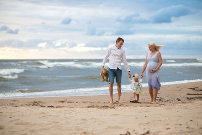 Full length of parents walking with baby girl at beach