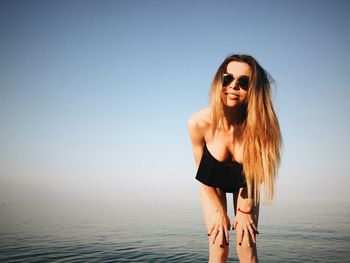 Portrait of beautiful woman wearing sunglasses at beach against clear blue sky