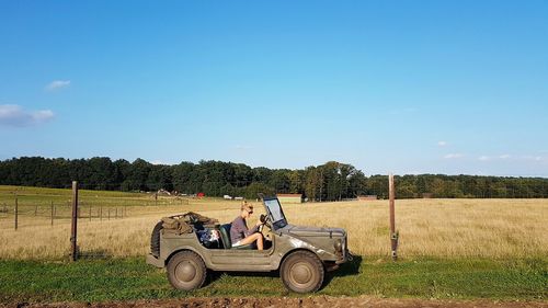 Side view of woman sitting in vehicle against blue sky