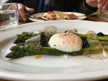 Close-up of poached egg with vegetables against man having food served on table