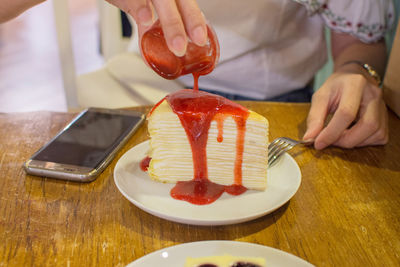Midsection of woman pouring syrup on cake slice in plate at table