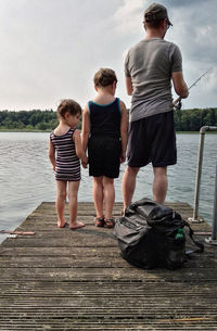 Rear view of family standing on pier while fishing in river