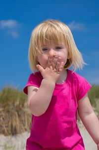 Portrait of cute girl covering mouth with hand against sky