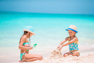 Rear view of women sitting on beach by sea
