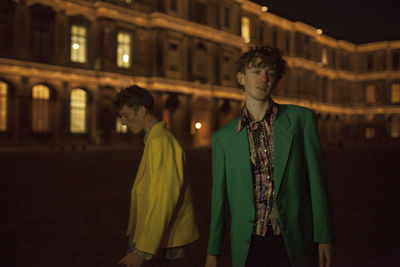 Young man standing against illuminated building at night