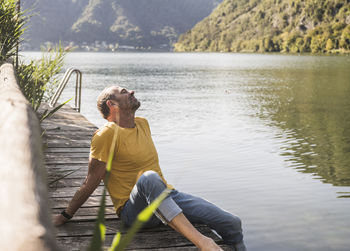 Man relaxing with eyes closed on jetty by lake