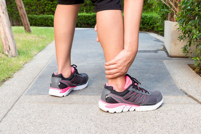 Low section of woman holding leg while standing on garden path