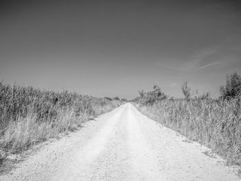 Empty road amidst field against sky