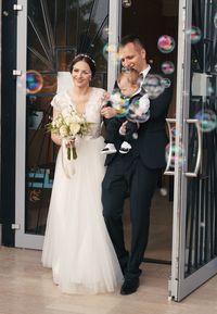 Just married couple with just baptized child going out of the church with soap bubbles in front