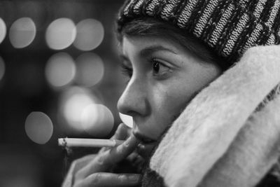 Side view of thoughtful young woman smoking cigarette against defocused lights