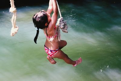 Girl wearing swimwear hanging on rope over river