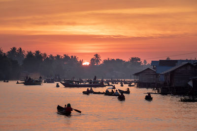 Silhouette houses on sea against orange sky