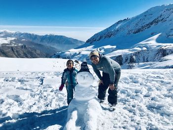 Portrait of father and son standing by snowman