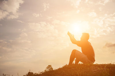 Side view of man sitting on land against sky during sunset