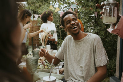 Happy young man eating salad and talking with friends in back yard party